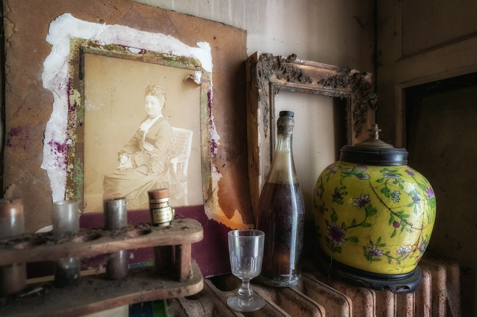 A framed portrait, glass vessels and a yellow floral vessel arranged on a shelf.